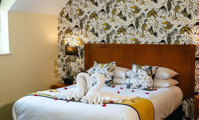 Hotel bedroom at Wild Pheasant Hotel & Spa with bed featuring towels folded into a swan shape, decorated with red rose petals.